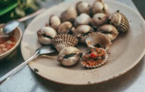 A delicious plate of cooked cockles served with sauce on the side, perfect for seafood lovers.