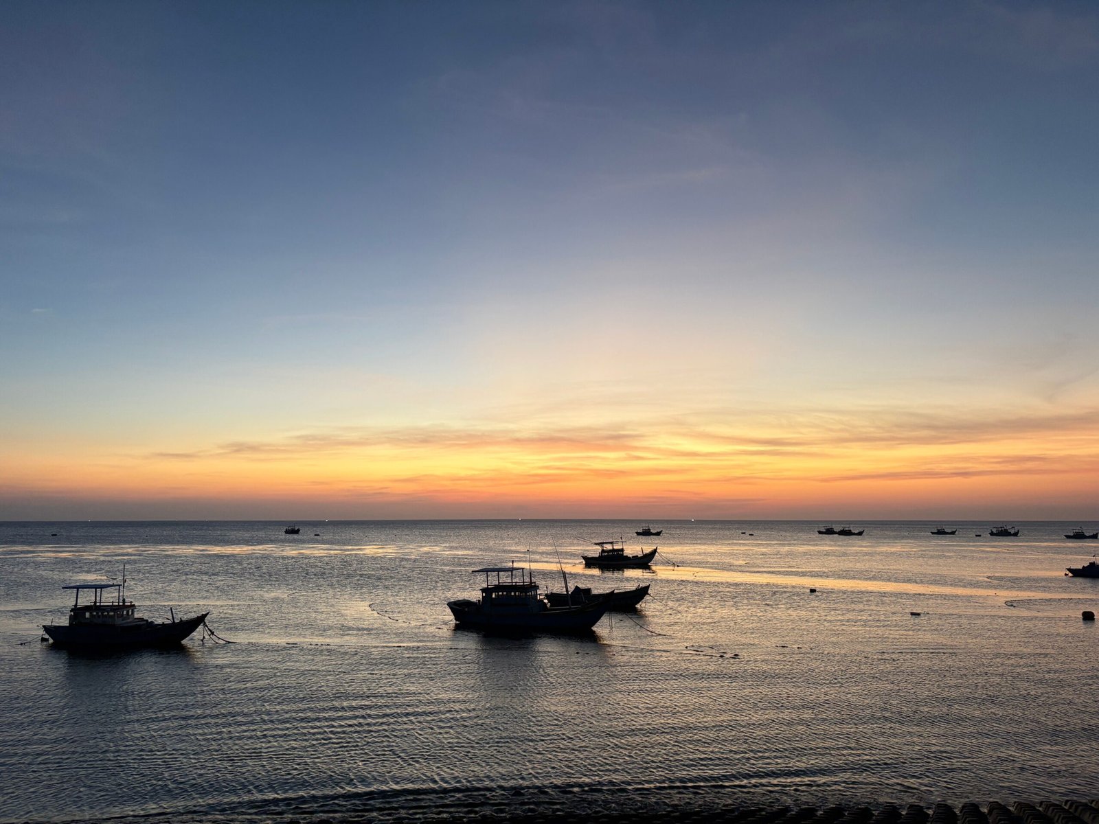 Serene sunset with fishing boats on the South China Sea, highlighting a warm, tranquil evening atmosphere.